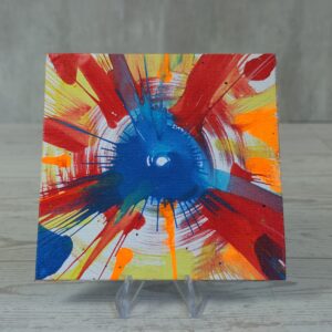 20260914_132729 Original 5x5 inch square abstract spin painting on canvas panel featuring a central cobalt blue circular burst with sharp splash lines surrounded by circular streaks of red, orange, yellow, and blue paint radiating outward toward the canvas edges, displayed on a clear stand.