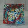 20260914_132927 Original 5x5 inch square abstract spin painting on canvas panel featuring fine, dense radial lines of crimson red, black, green, and blue spinning outward from a bright yellow and white speckled core, shown on a clear acrylic stand.