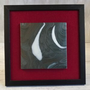 Framed acrylic pour painting, charcoal and slate gray abstract with two curved white shapes, 5x5 canvas on red felt in black wood-grain frame, front view