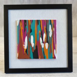 Framed acrylic drip pour painting, vertical streaks of teal magenta orange copper and black with white shapes, 5x5 canvas on white felt in black wood-grain frame, front view