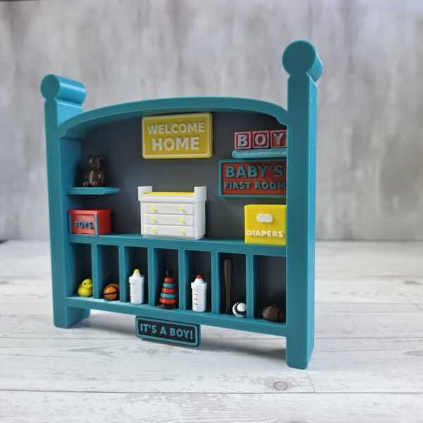 20261020_153209 Crib-shaped nursery shadow box in teal and misty blue with red, yellow, and white miniatures, left angle view