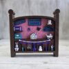 20261020_153232 Crib-shaped nursery shadow box in brown and pink with purple, teal, and white miniatures, front view