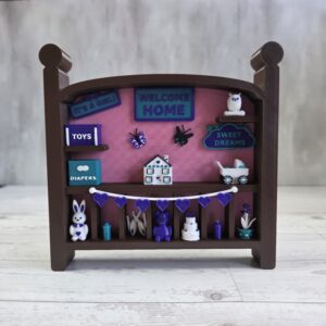 Crib-shaped nursery shadow box in brown and pink with purple, teal, and white miniatures, front view