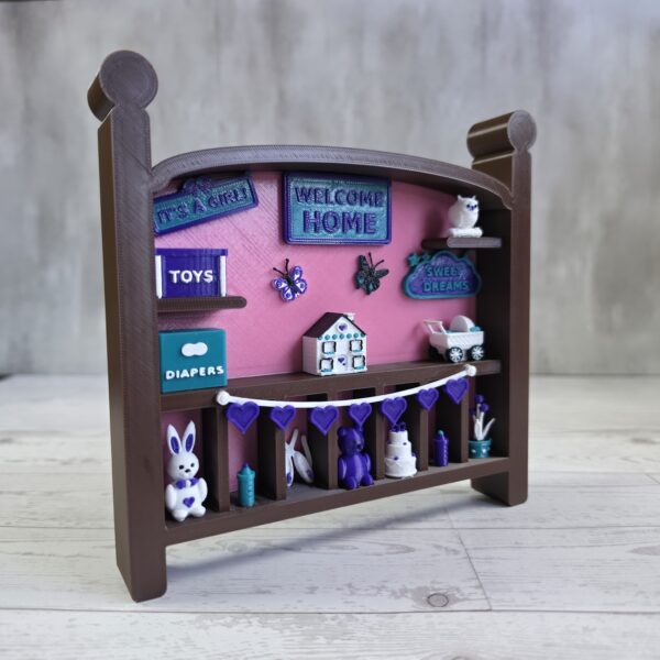 20261020_153246 Crib-shaped nursery shadow box in brown and pink with purple, teal, and white miniatures, right angle view