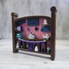 20261020_153311 Crib-shaped nursery shadow box in brown and pink with purple, teal, and white miniatures, left angle view