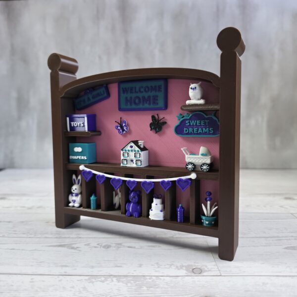 20261020_153311 Crib-shaped nursery shadow box in brown and pink with purple, teal, and white miniatures, left angle view